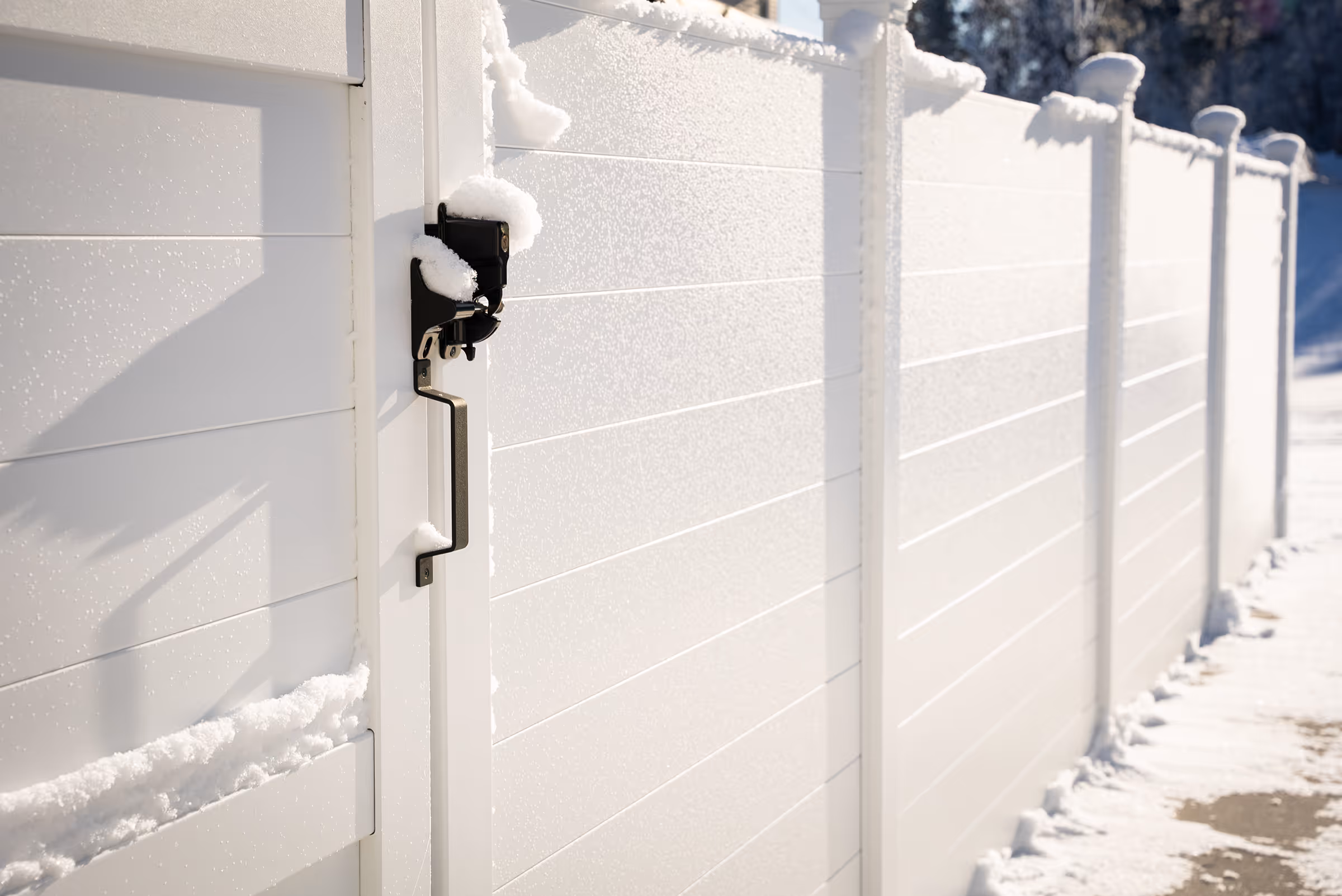 White aluminum fence covered with snow along a snowy pathway under sunlight.
