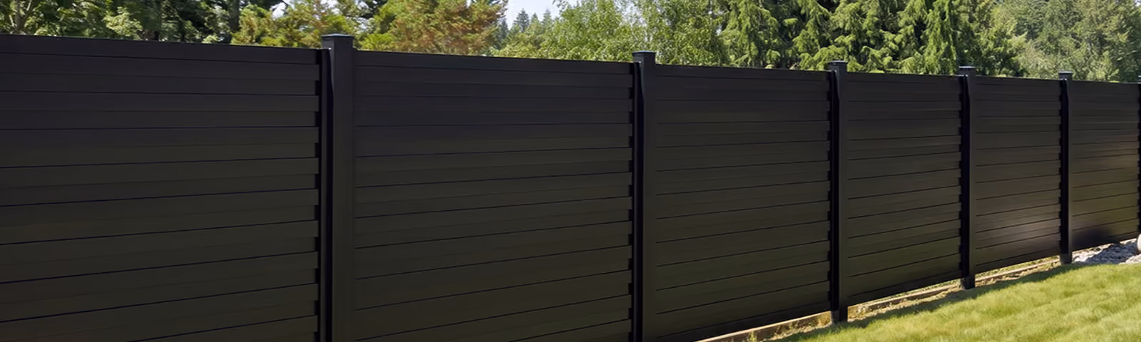 Long black aluminum privacy fence with horizontal panels outdoors near green trees and grass.