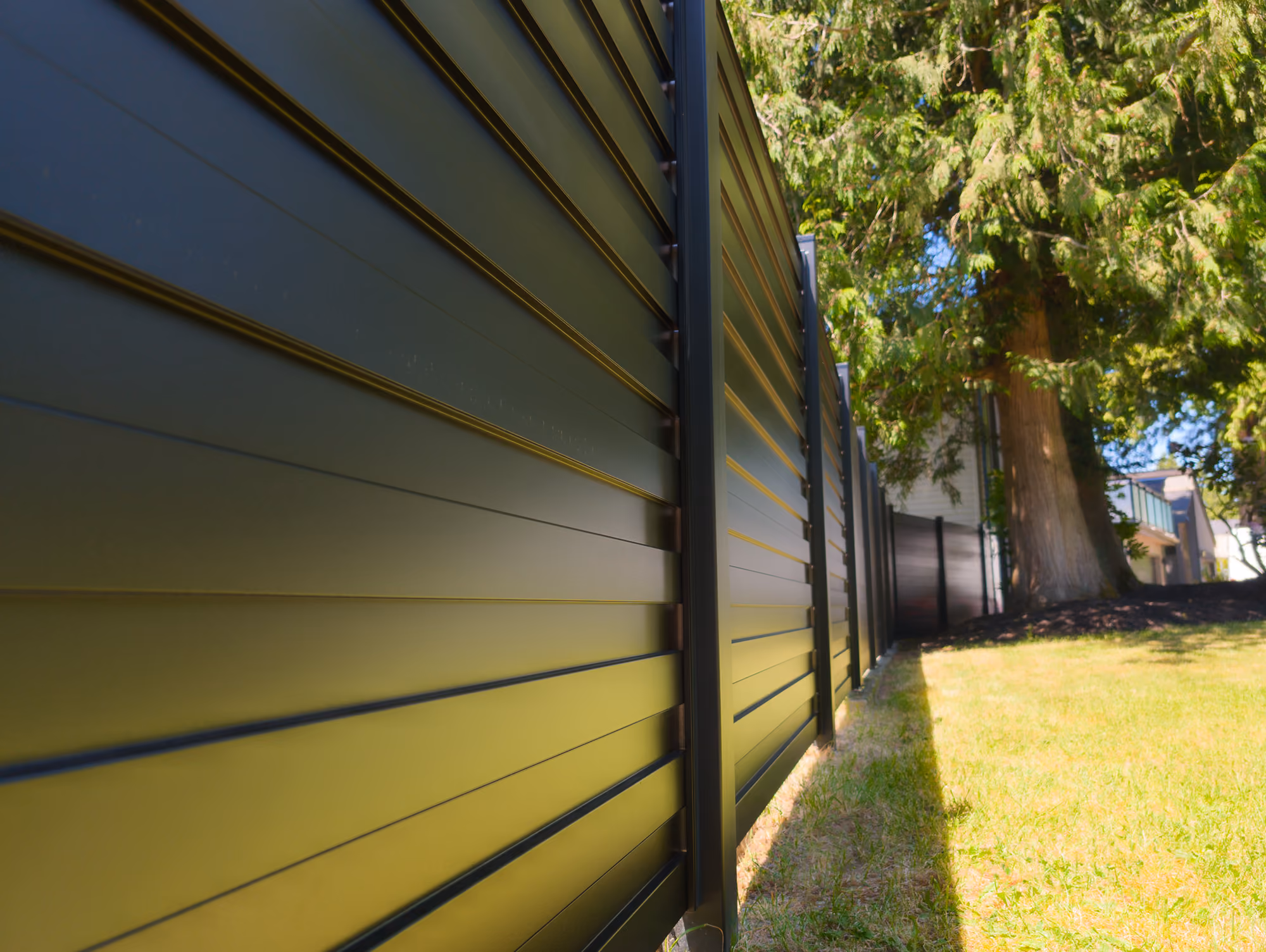 Modern black horizontal metal fence along a green lawn with trees and houses in background.
