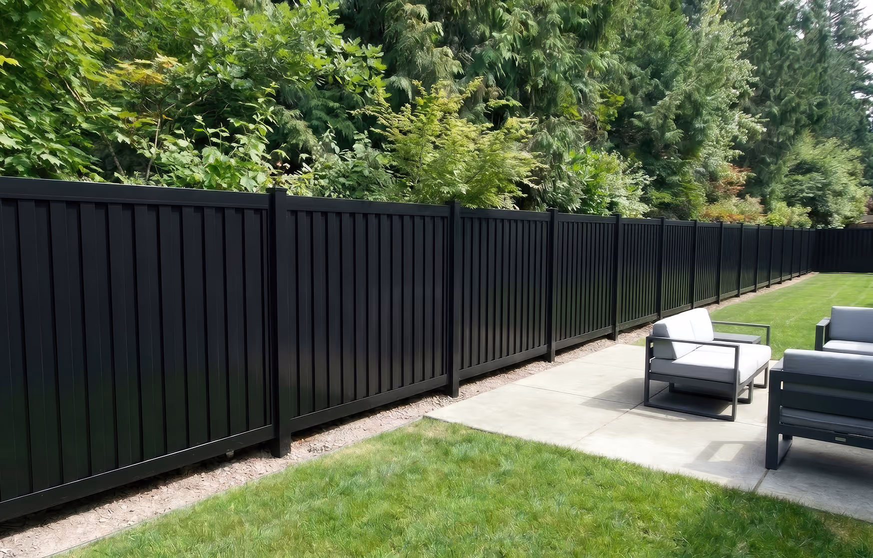 Long black vertical panel aluminum fence bordering a backyard with patio furniture and green lawn.