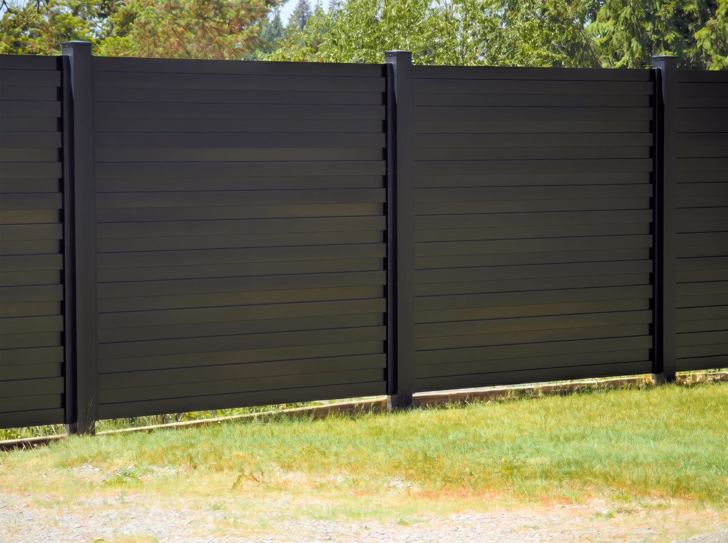 Modern black horizontal slat fence panels in a green yard with trees in the background.