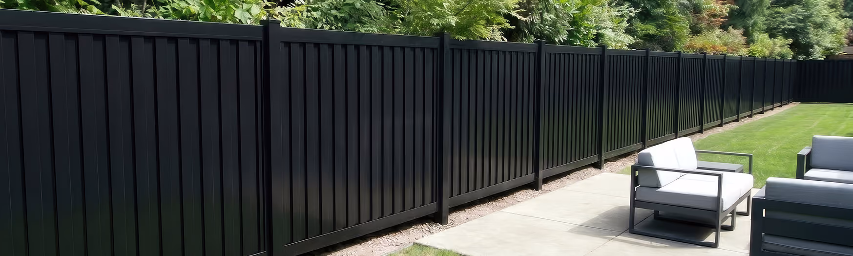 Long black vertical shadow box aluminum fence with outdoor patio seating and green lawn.