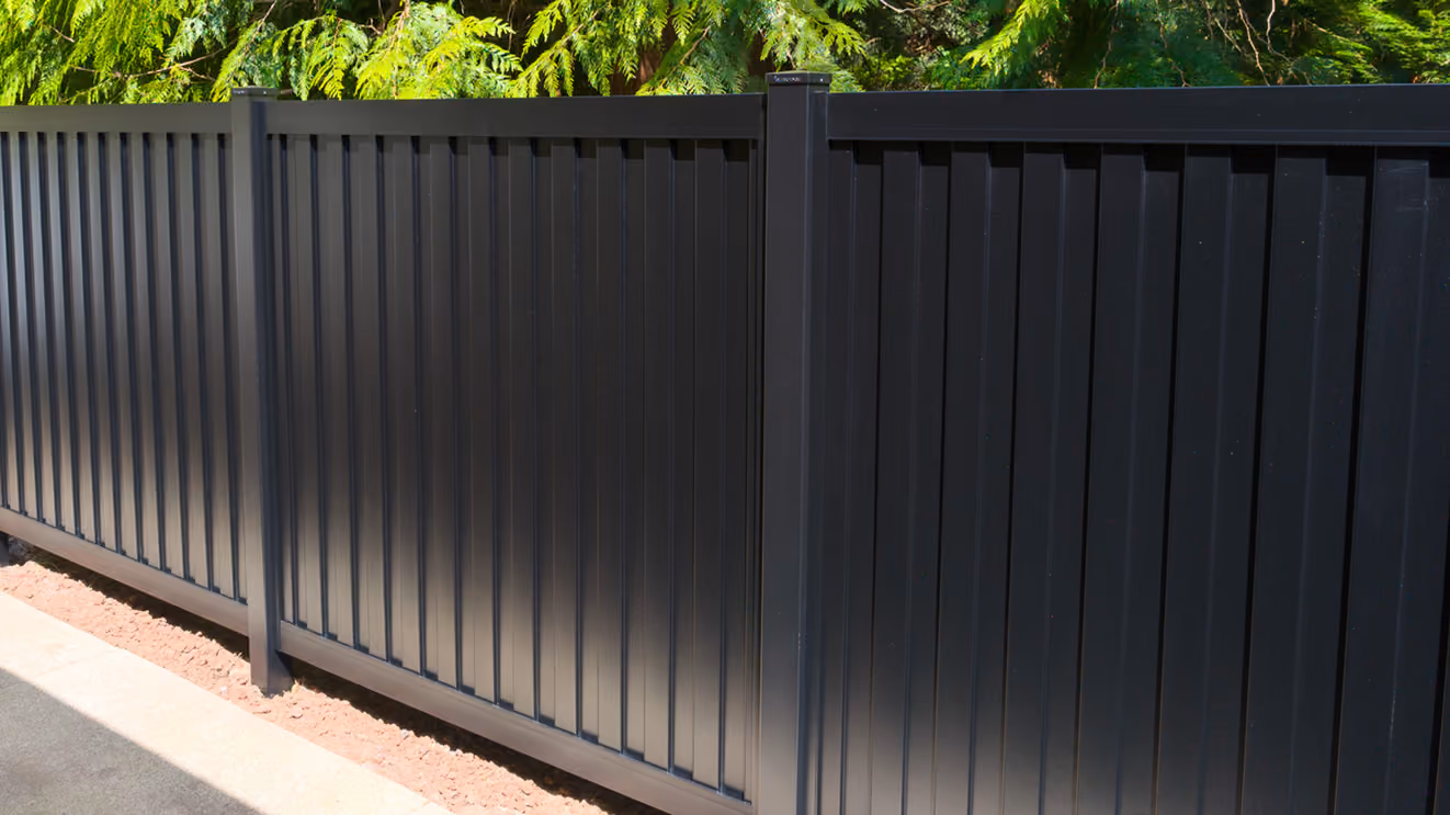 Modern black vertical panel fence with posts outside, greenery in background.