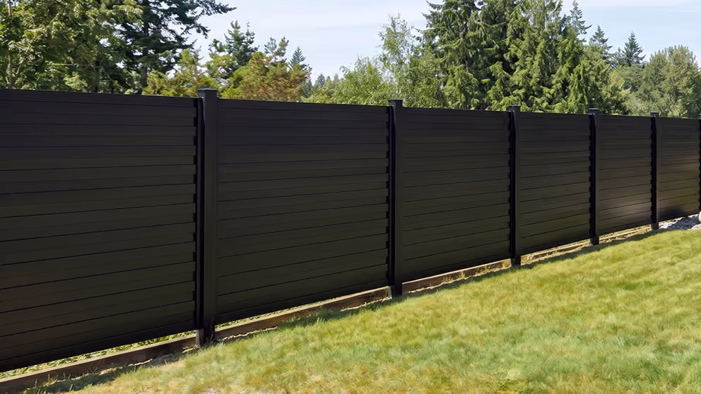 Long black horizontal slat aluminum fence along a green grassy yard with trees in the background.