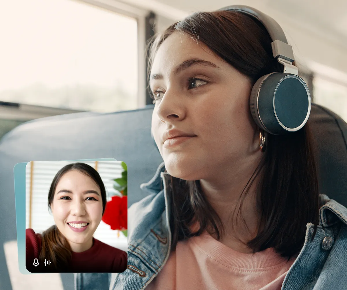 Young woman wearing headphones looking out a window with a video call screen showing a smiling woman in the corner.