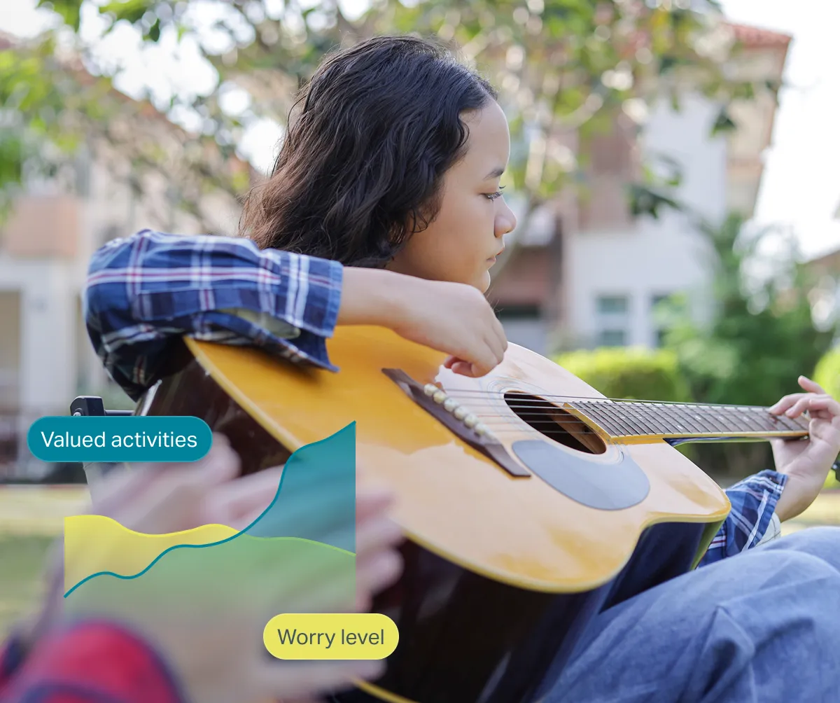 Teen girl playing an acoustic guitar outdoors in a garden or yard.