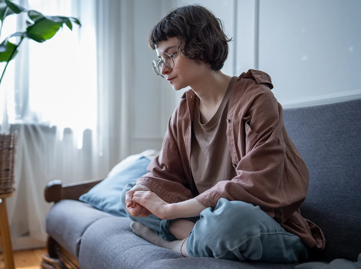 Girl with long brown hair sitting on couch daydreaming