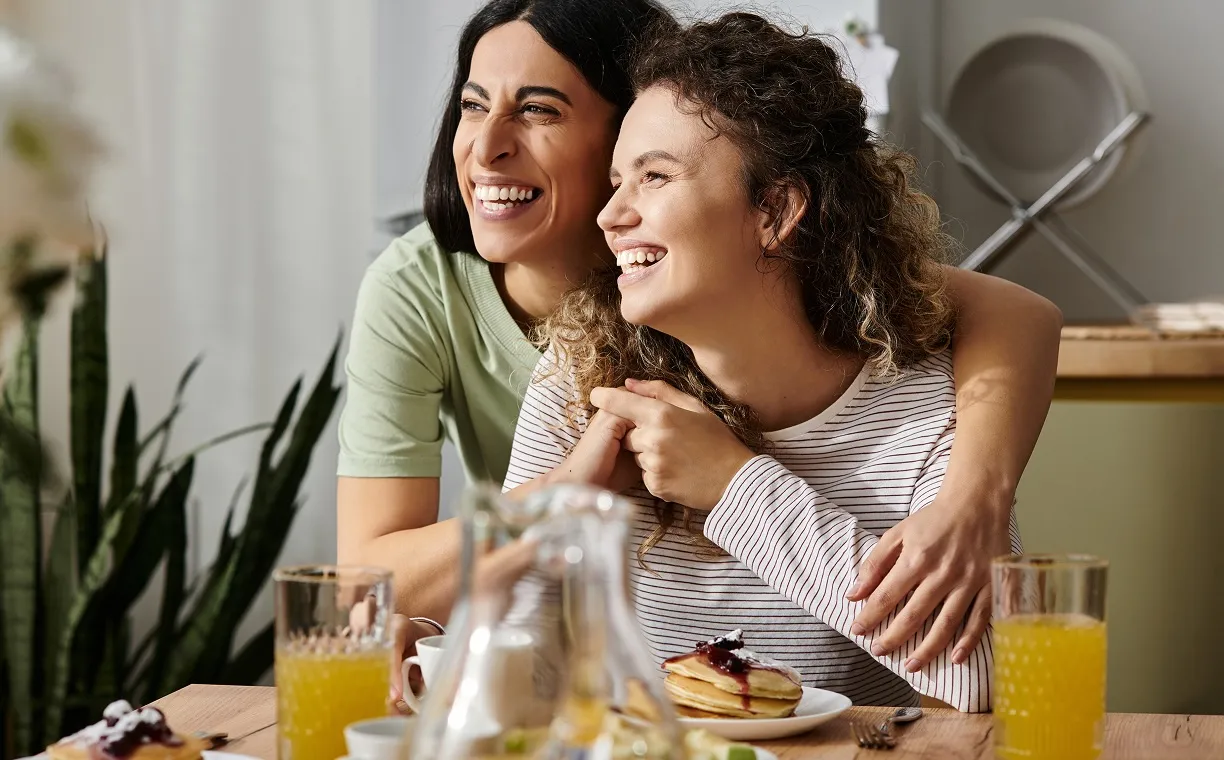 Smiling girl with glasses hugging an adult wearing a green shirt in a cozy indoor setting.