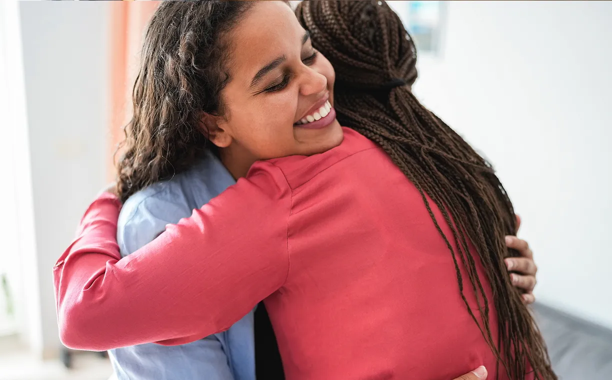 Smiling girl with glasses hugging an adult wearing a green shirt in a cozy indoor setting.