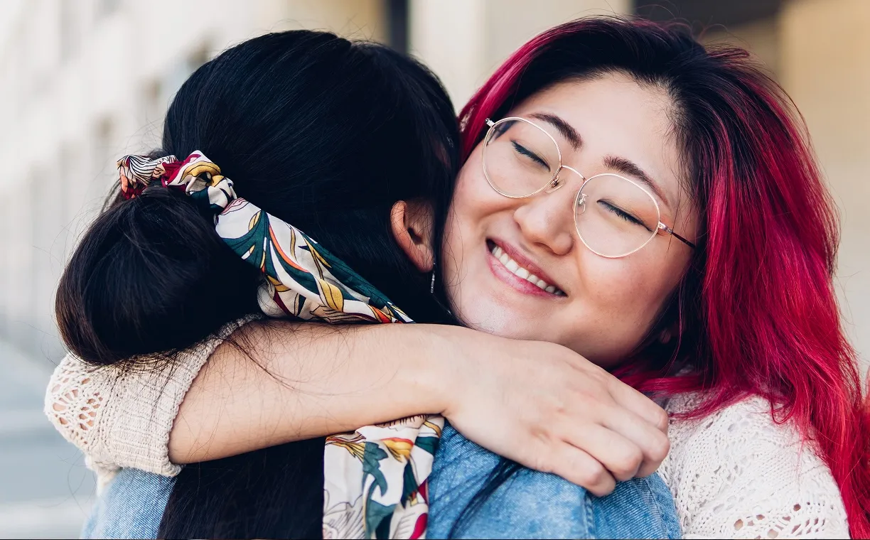 Smiling girl with glasses hugging an adult wearing a green shirt in a cozy indoor setting.