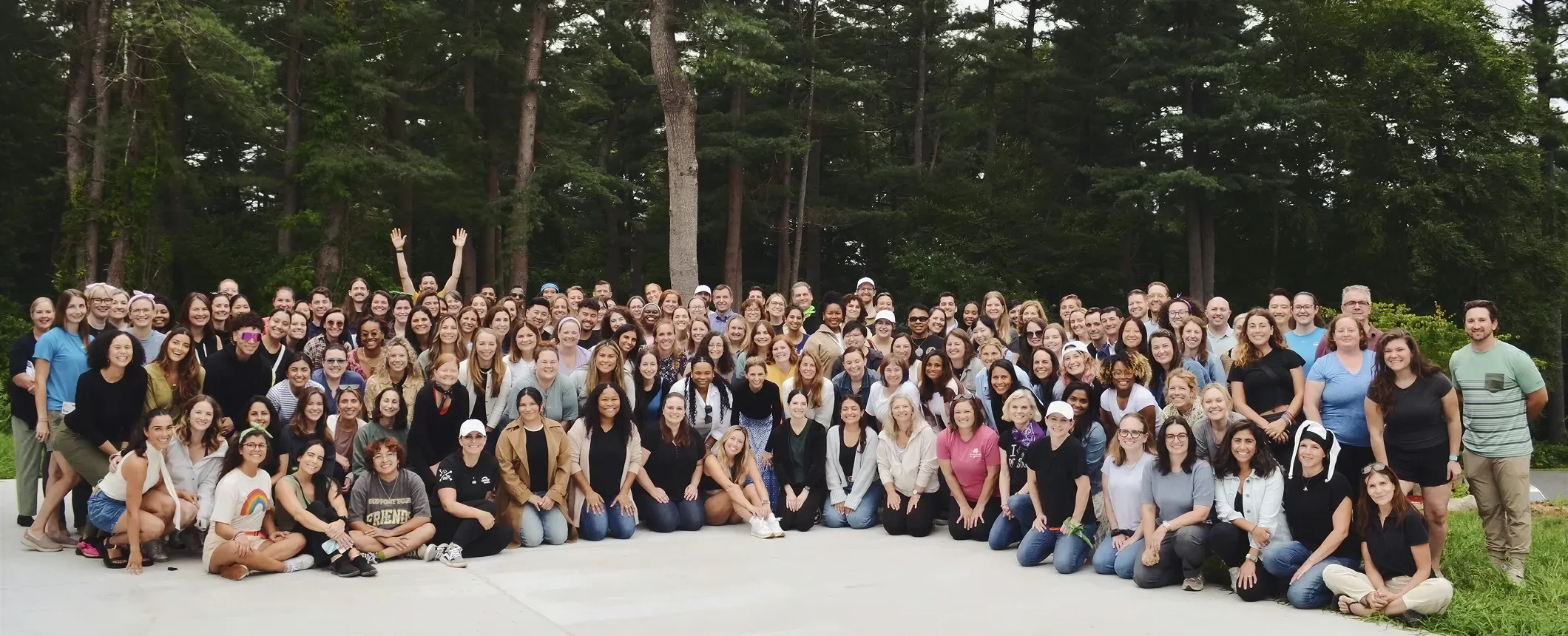 Large diverse group of people posing for a group photo outdoors with trees in the background.
