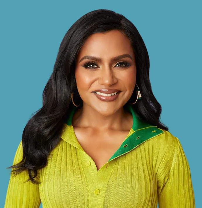 Smiling woman with long black hair wearing gold hoop earrings and a yellow-green collared top against a blue background.