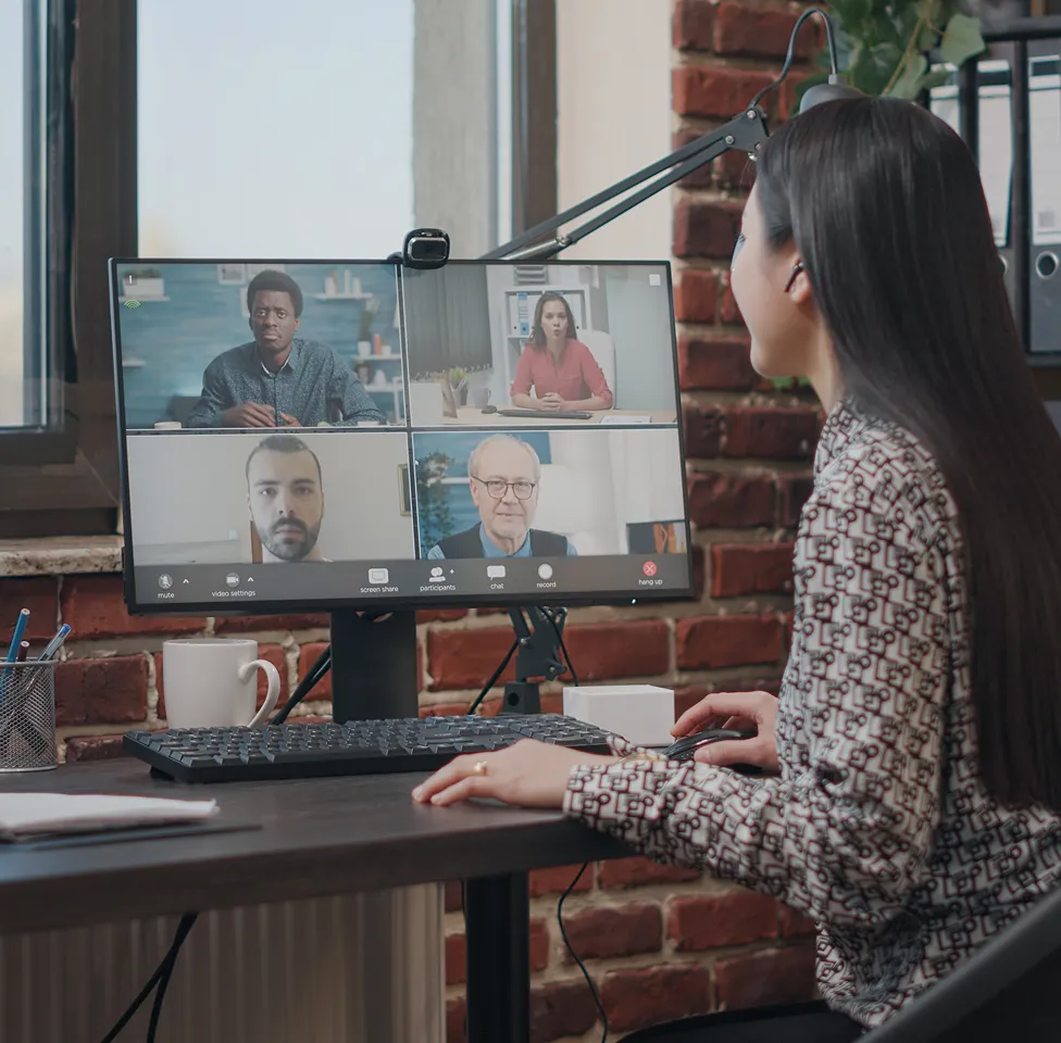 Woman attending a video conference on a desktop computer with four colleagues visible on the screen.