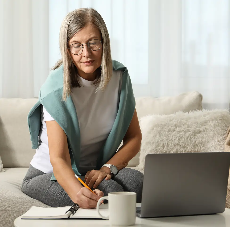 Smiling female doctor in white coat typing on a laptop at a desk in a bright office.