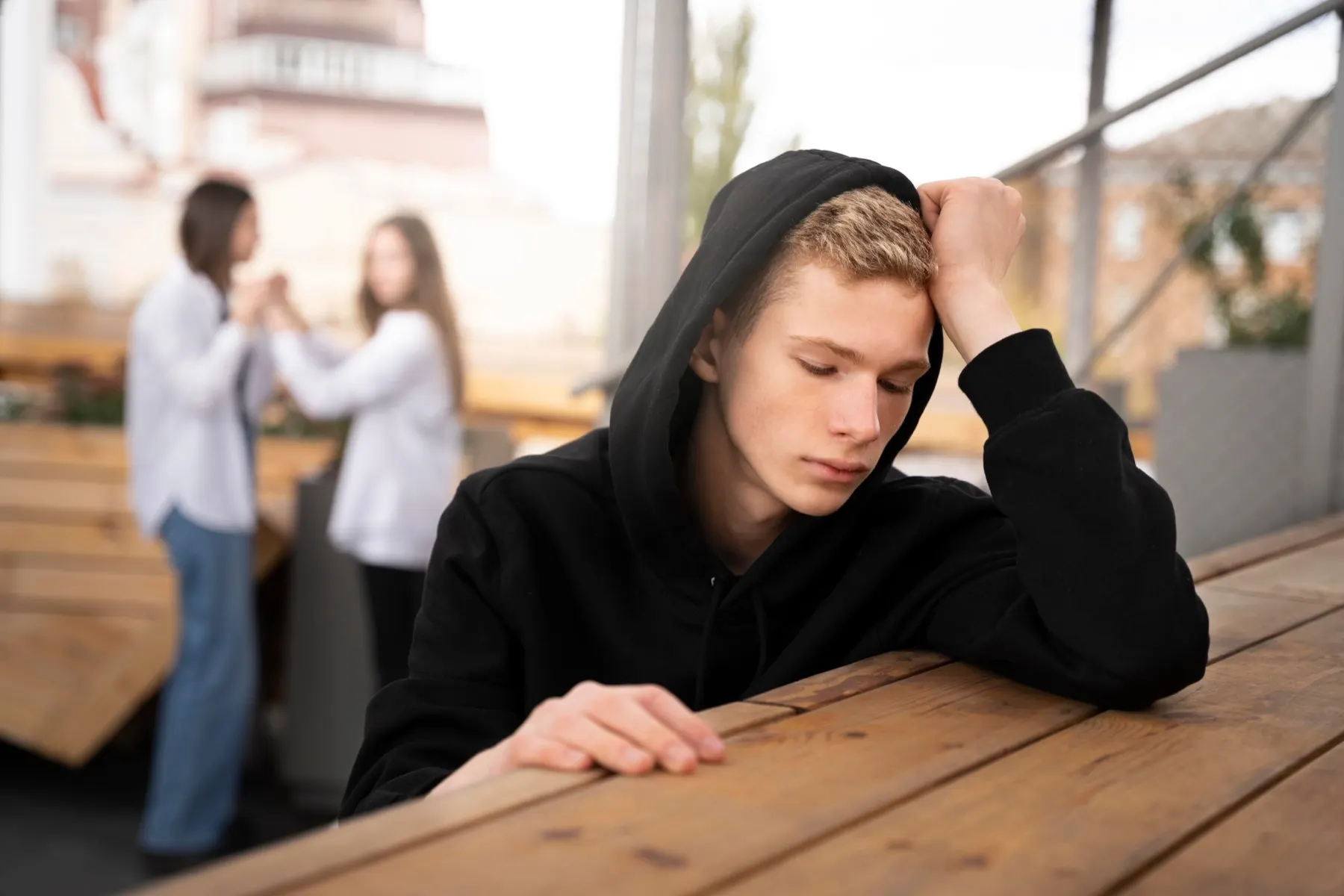Teen boy in a hoodie resting his head on his hand at an outdoor table