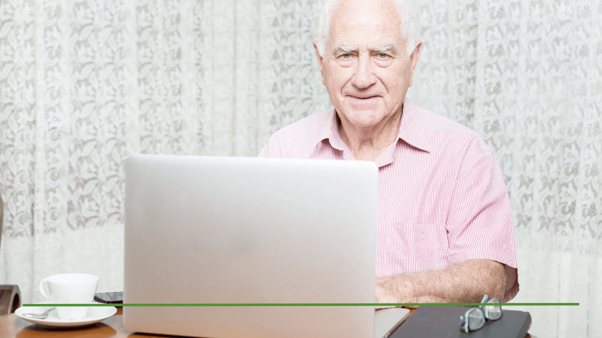 Senior man working on a laptop at home, representing someone who continues working full time while collecting Social Security at age 70.