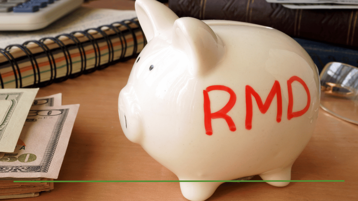 Are taxes taken out of your RMD illustrated by a white piggy bank labeled RMD in red marker, sitting on a desk beside cash, a calculator, and a notebook