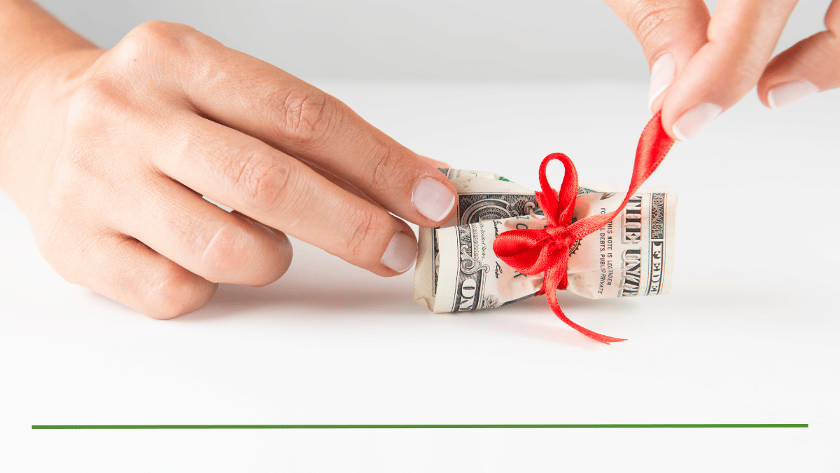 Hand tying a red ribbon around rolled cash, illustrating the question of whether you can gift your RMD to family