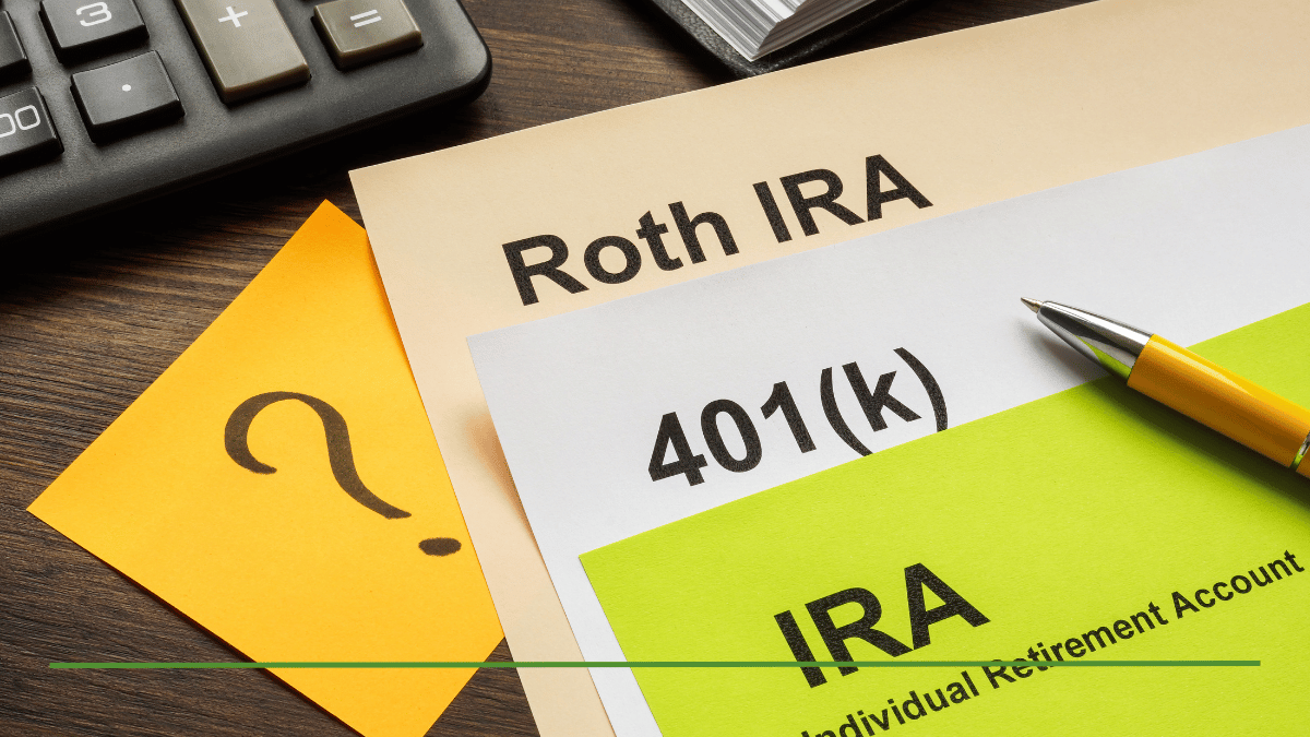 Papers labeled Roth IRA, 401(k), and IRA (Individual Retirement Account) on a desk with a calculator, pen, and question mark sticky note