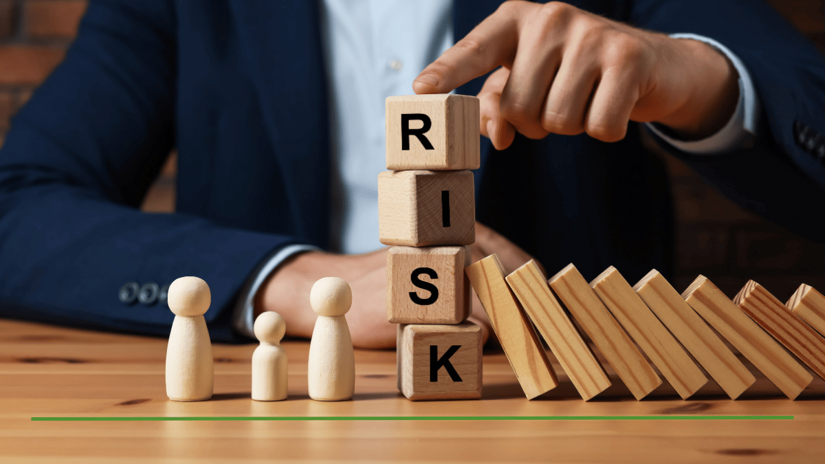 Businessman stacking wooden blocks spelling 'RISK' beside falling dominoes, illustrating how risky a Roth IRA really is