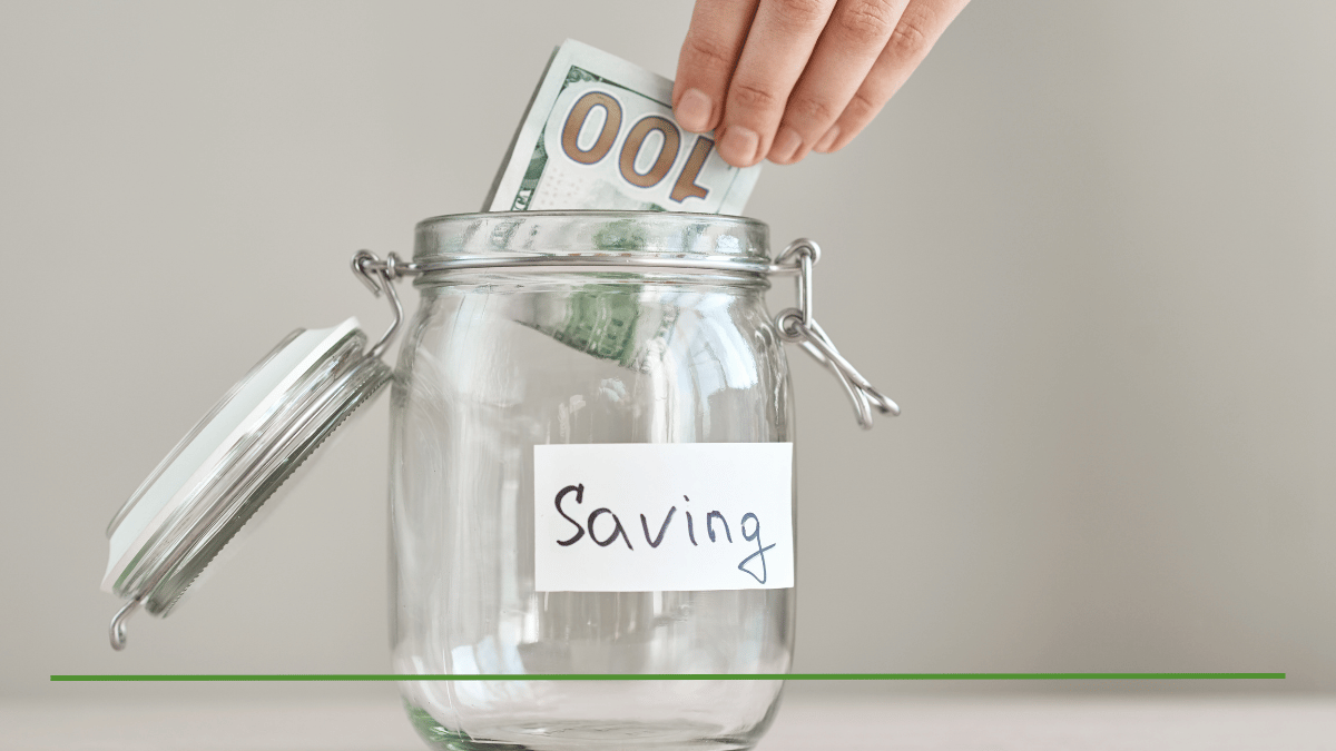 Hand placing a $100 bill into a glass savings jar labeled 'Saving,' representing the choice between a CD and an IRA for growing savings