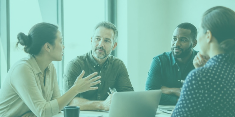 A team member speaking up in a meeting while her manager and colleagues listen
