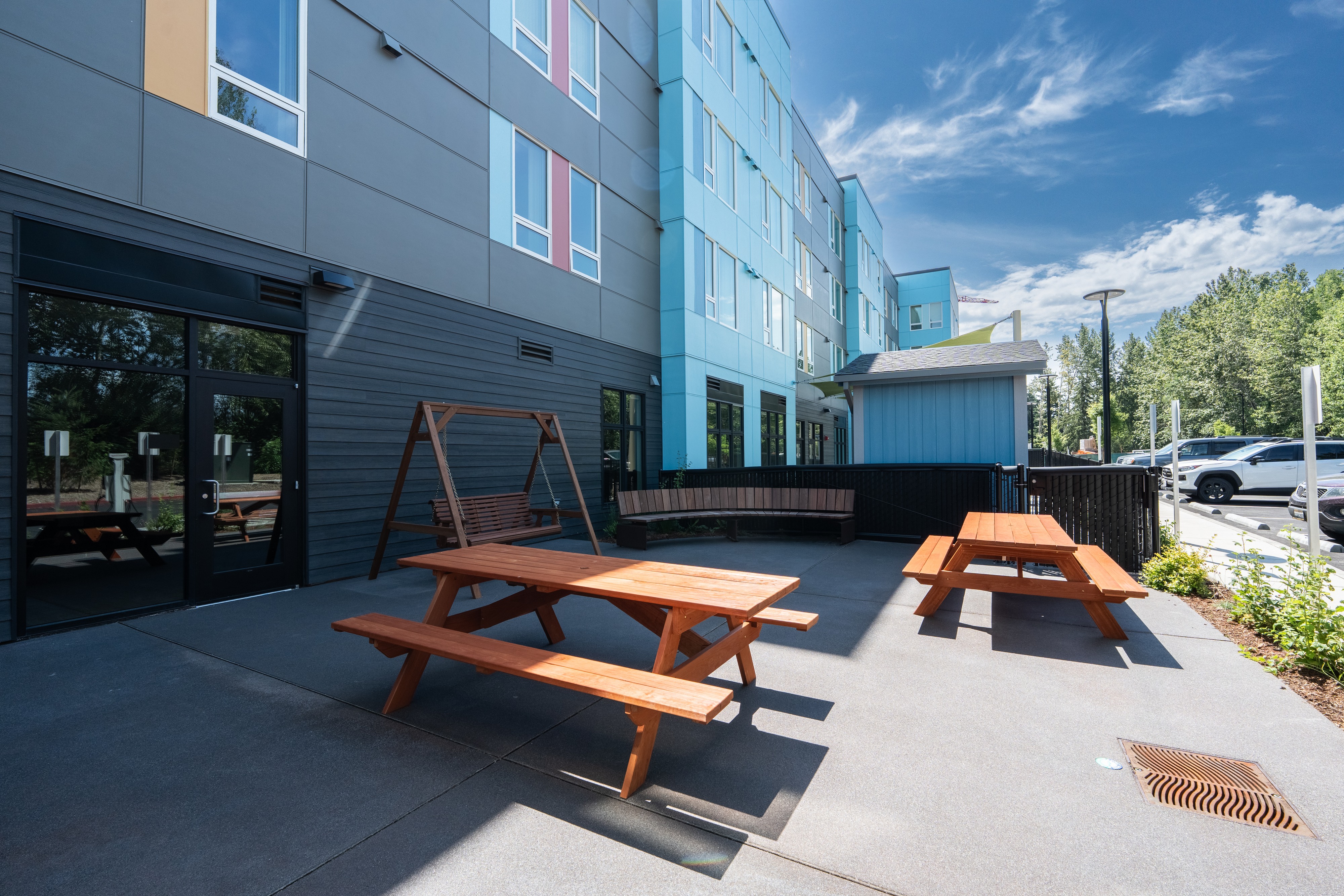 Outdoor patio with cedar picnic tables and a bench swing at Bellis Fair Family Housing