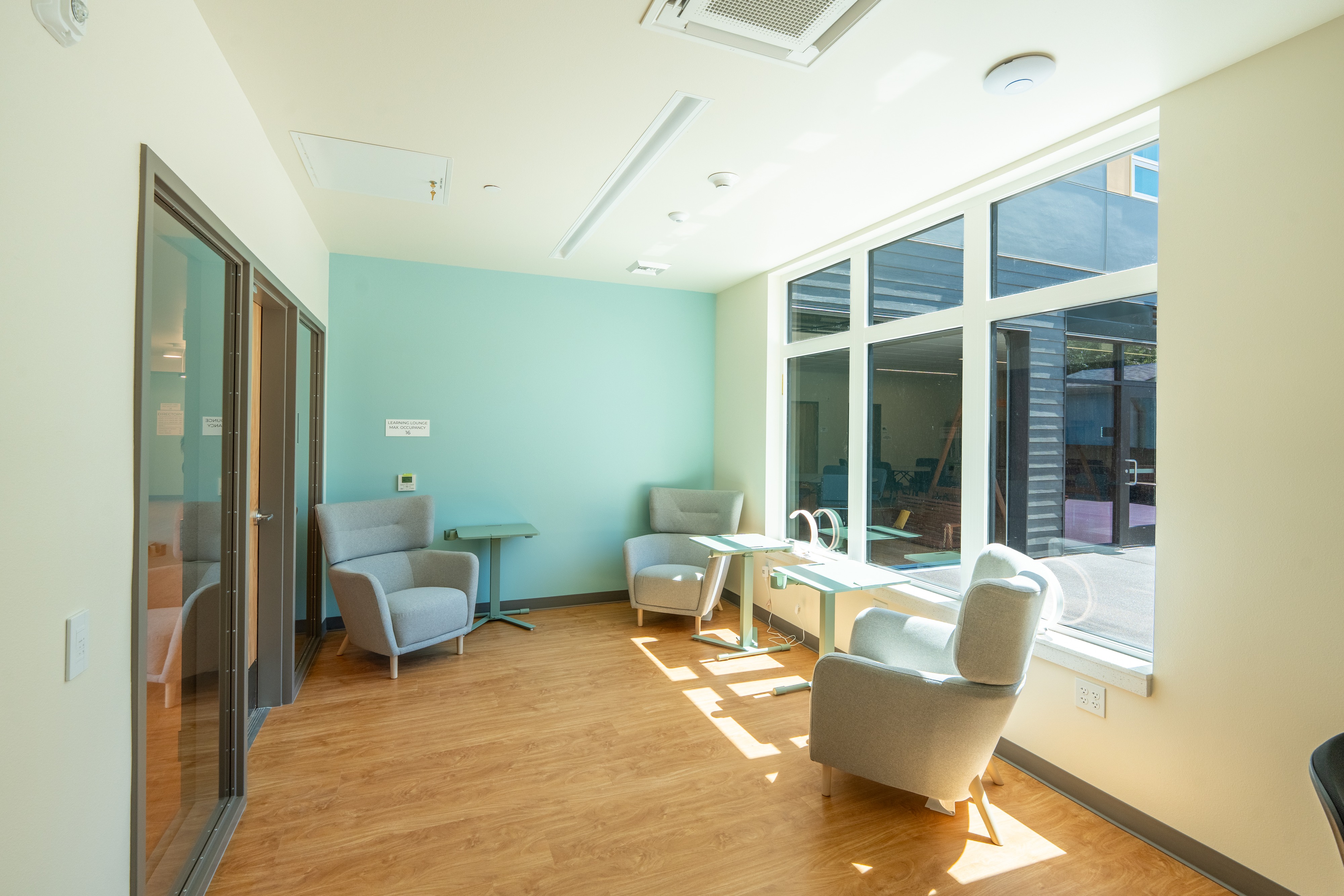 Resident lounge with armchairs and courtyard views at Bellis Fair Family Housing