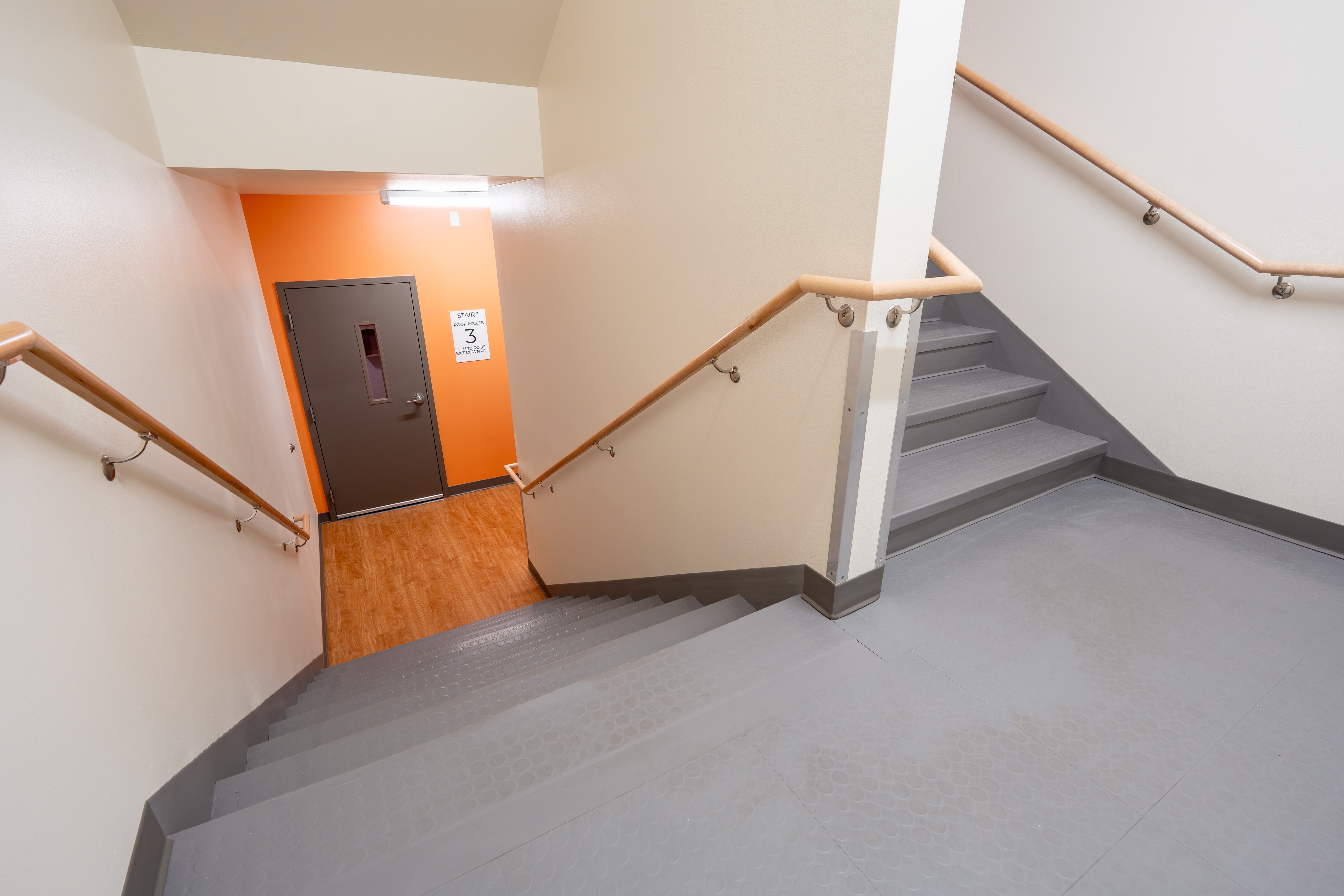 Stairwell with wood handrails and orange accent wall at Bellis Fair Family Housing