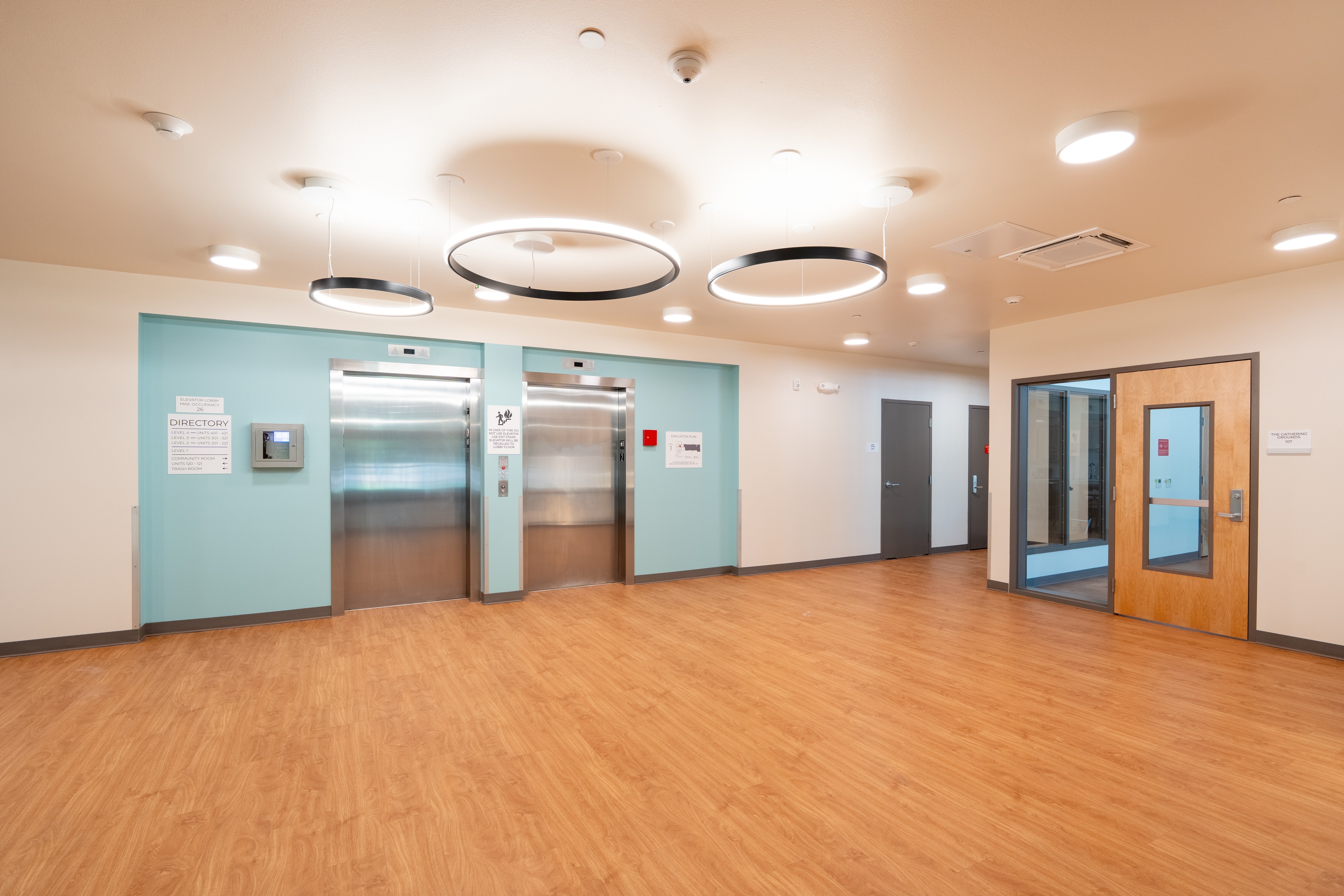 Elevator lobby with teal accent wall and ring pendant lights at Bellis Fair Family Housing