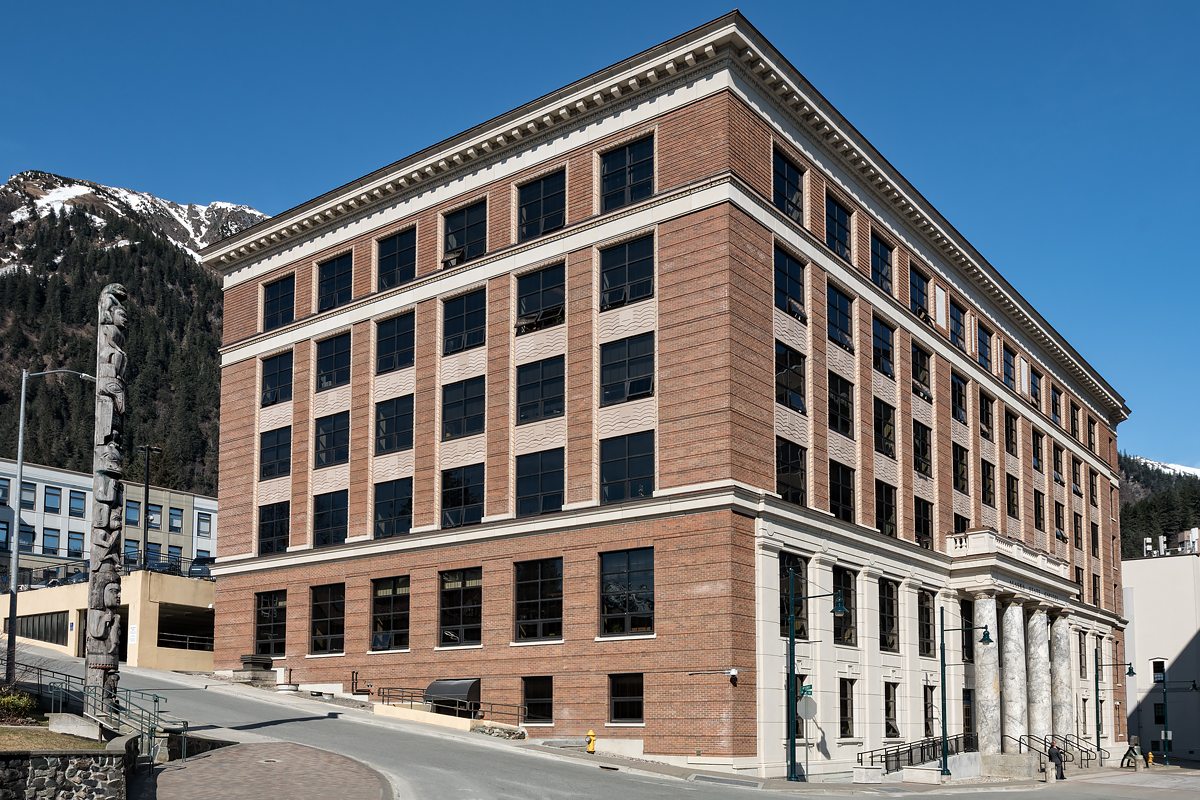 Renovated Alaska State Capitol with totem pole and snow-capped peaks in downtown Juneau