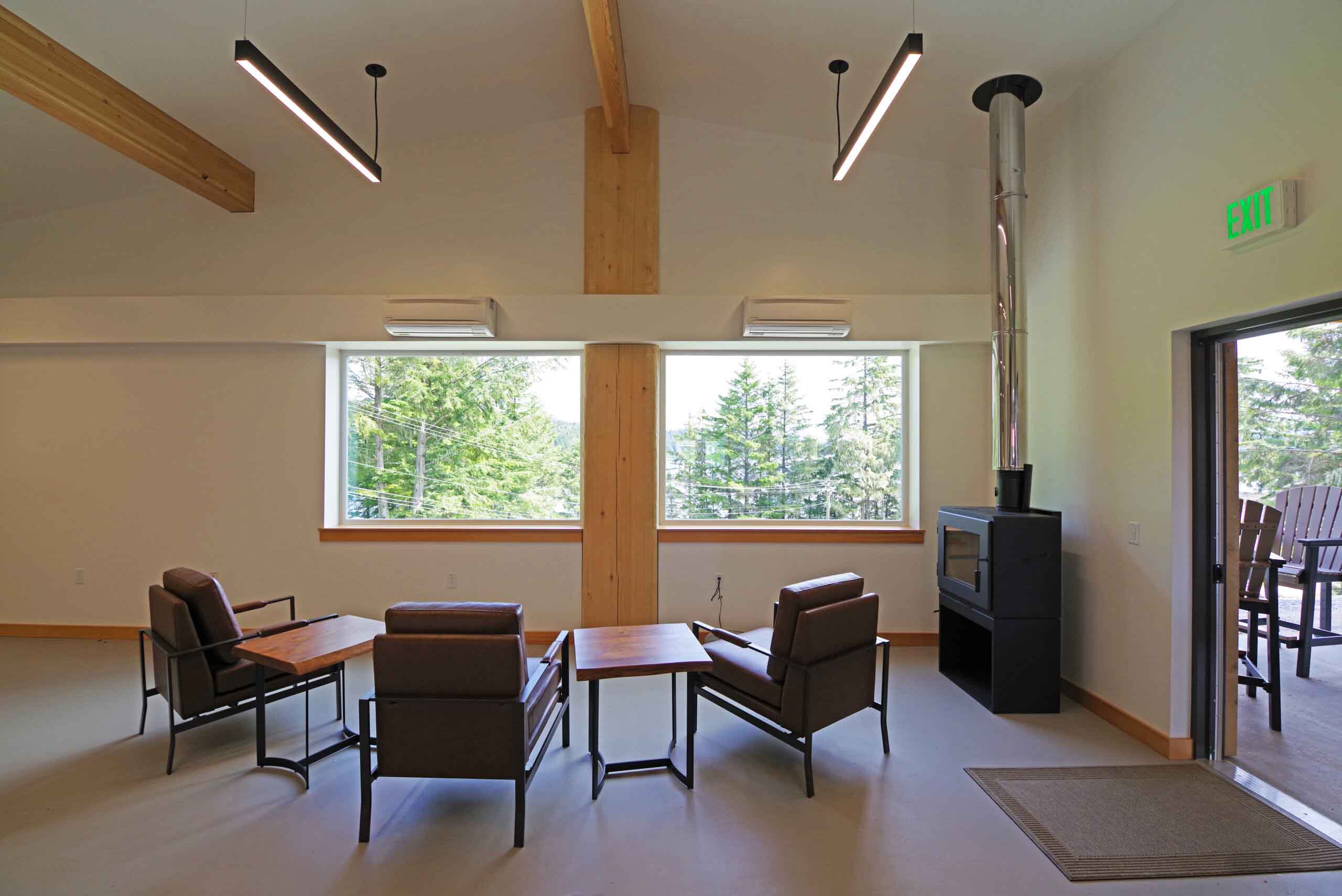 Wood stove lounge with forest-view windows inside the Angoon Visitor Center