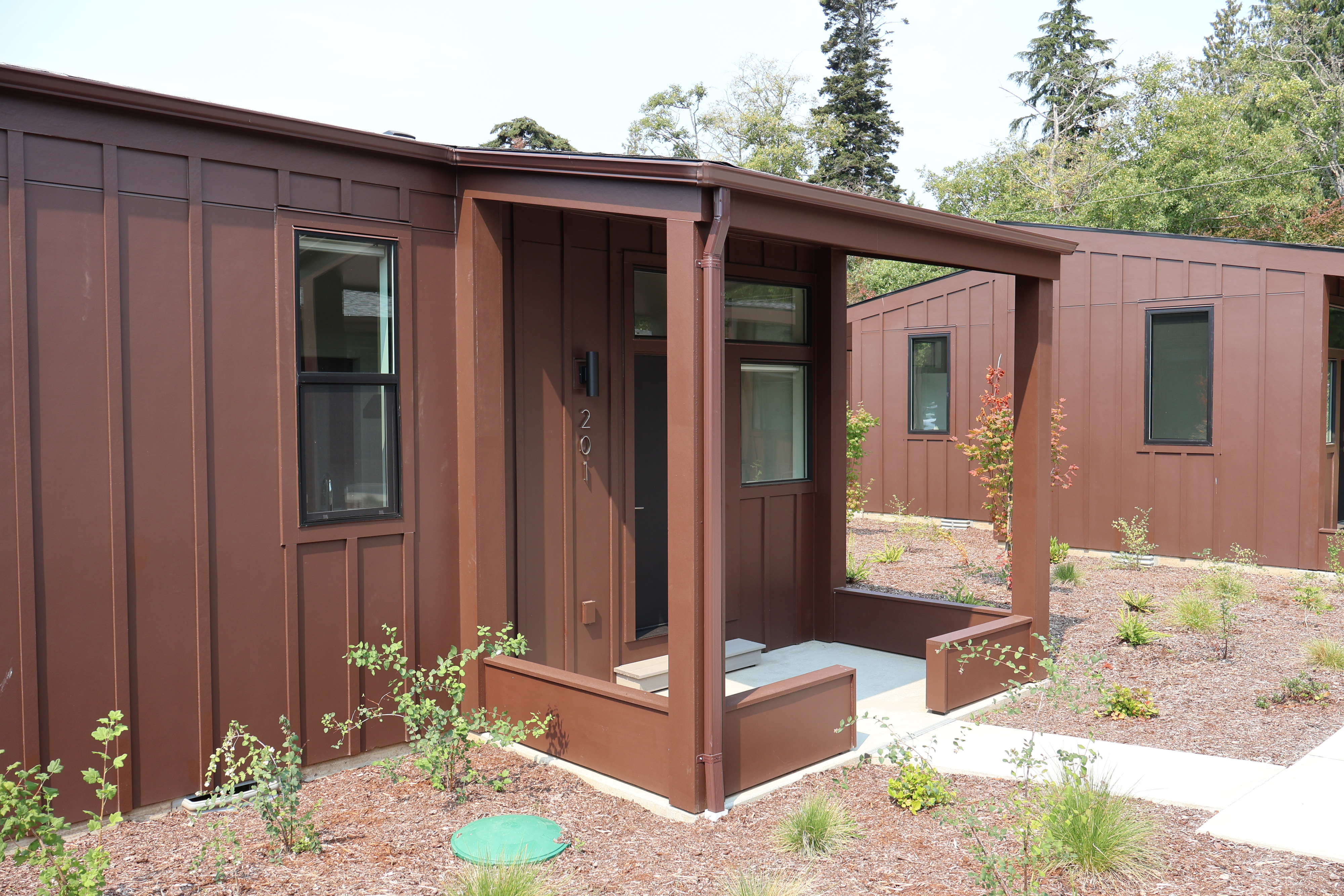 Covered entries and porches on adjoining tiny homes at Crowberry Mini Homes, with new plantings along the walkway
