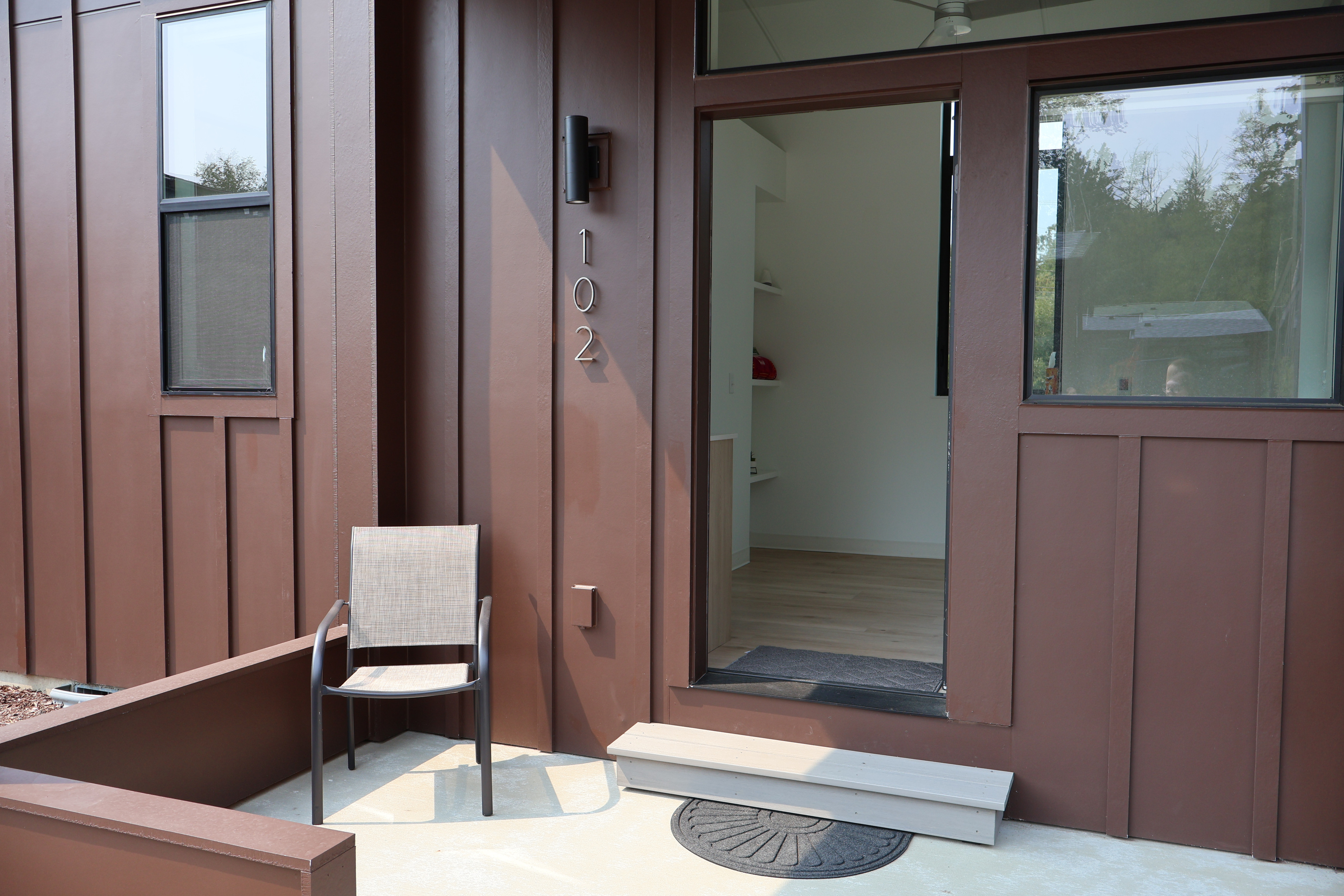 The open front door of unit 102 at Crowberry Mini Homes, showing the finished interior, with a chair on the covered porch