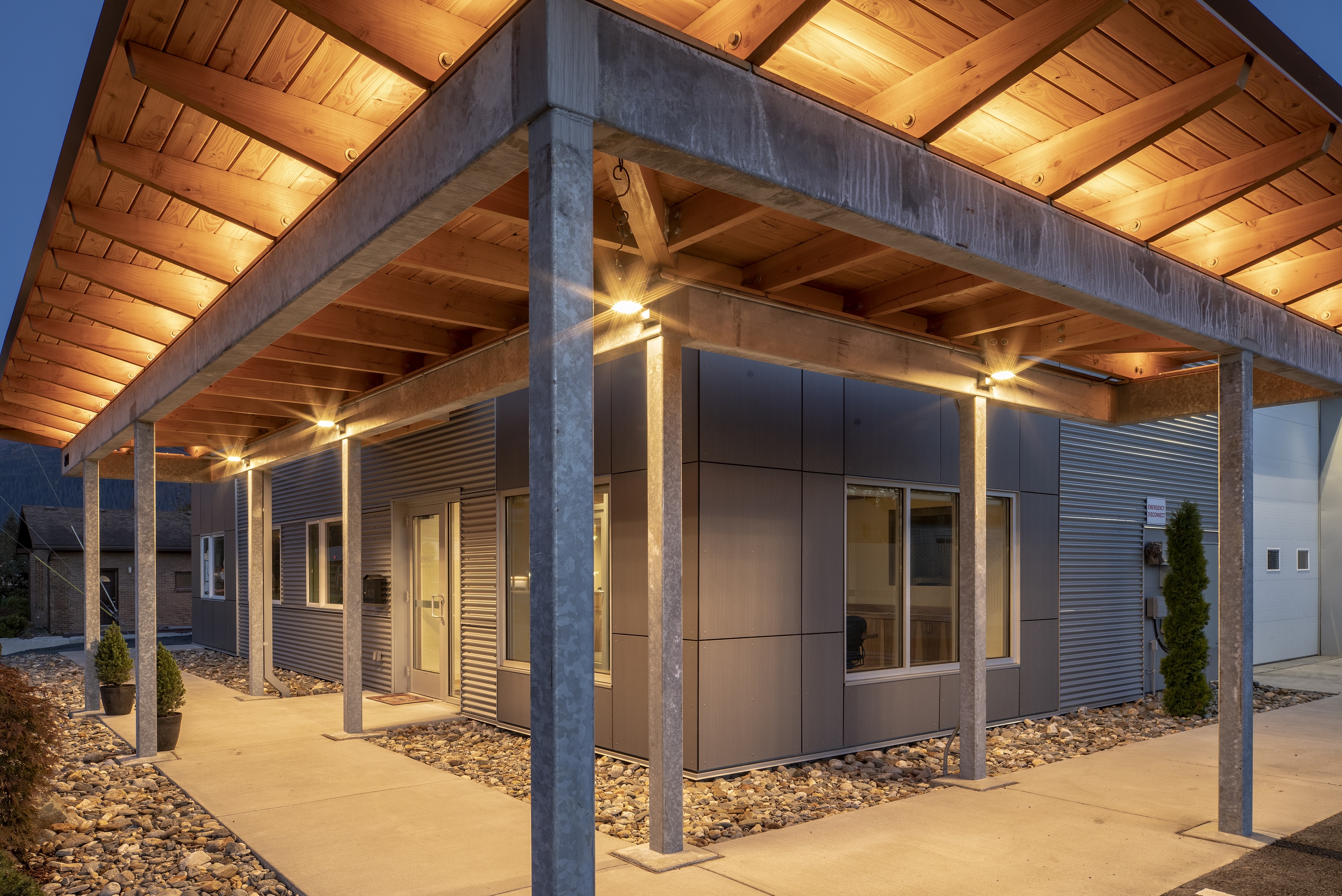 Lit timber canopy and galvanized steel colonnade wrapping the entry of Dawson's Juneau headquarters at dusk