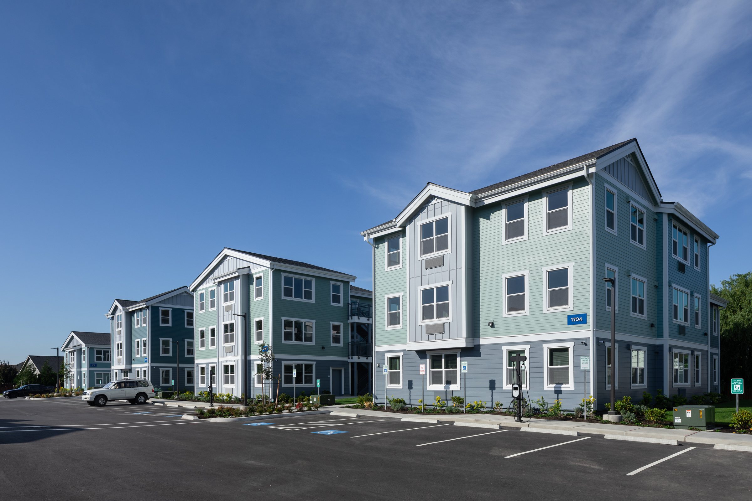 Apartment buildings across the parking lot at Ballington Flats, with an EV charger and landscaping