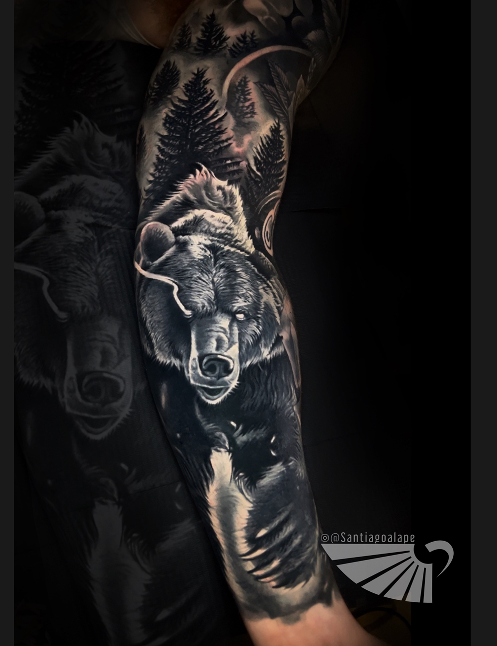 Black and grey realism sleeve tattoo of a bear in a pine forest under the moon by Santiago