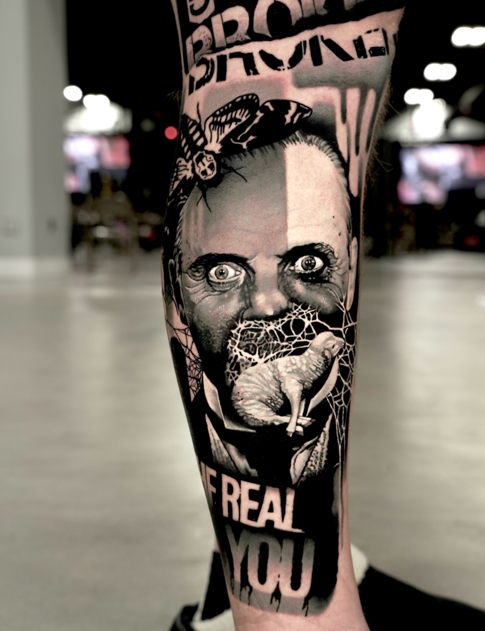 Black and grey realism leg tattoo of Hannibal Lecter with a moth and lamb by Juanky