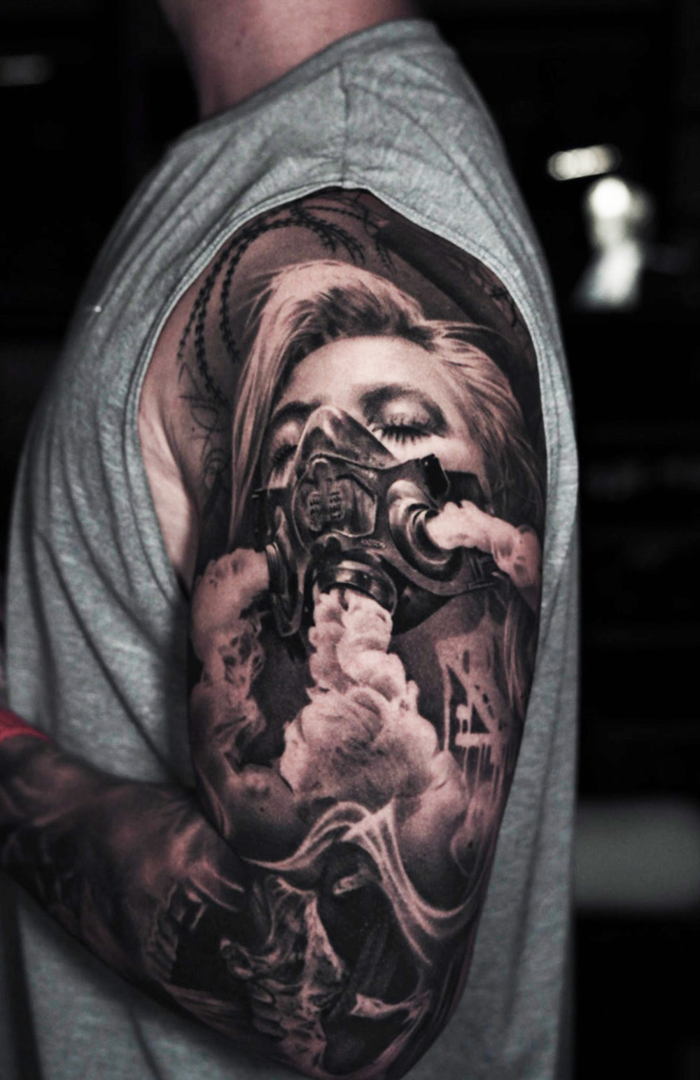 Black and grey realism tattoo of a woman in a gas mask exhaling smoke on the upper arm at The Secret Tattoo Studio in Tampa