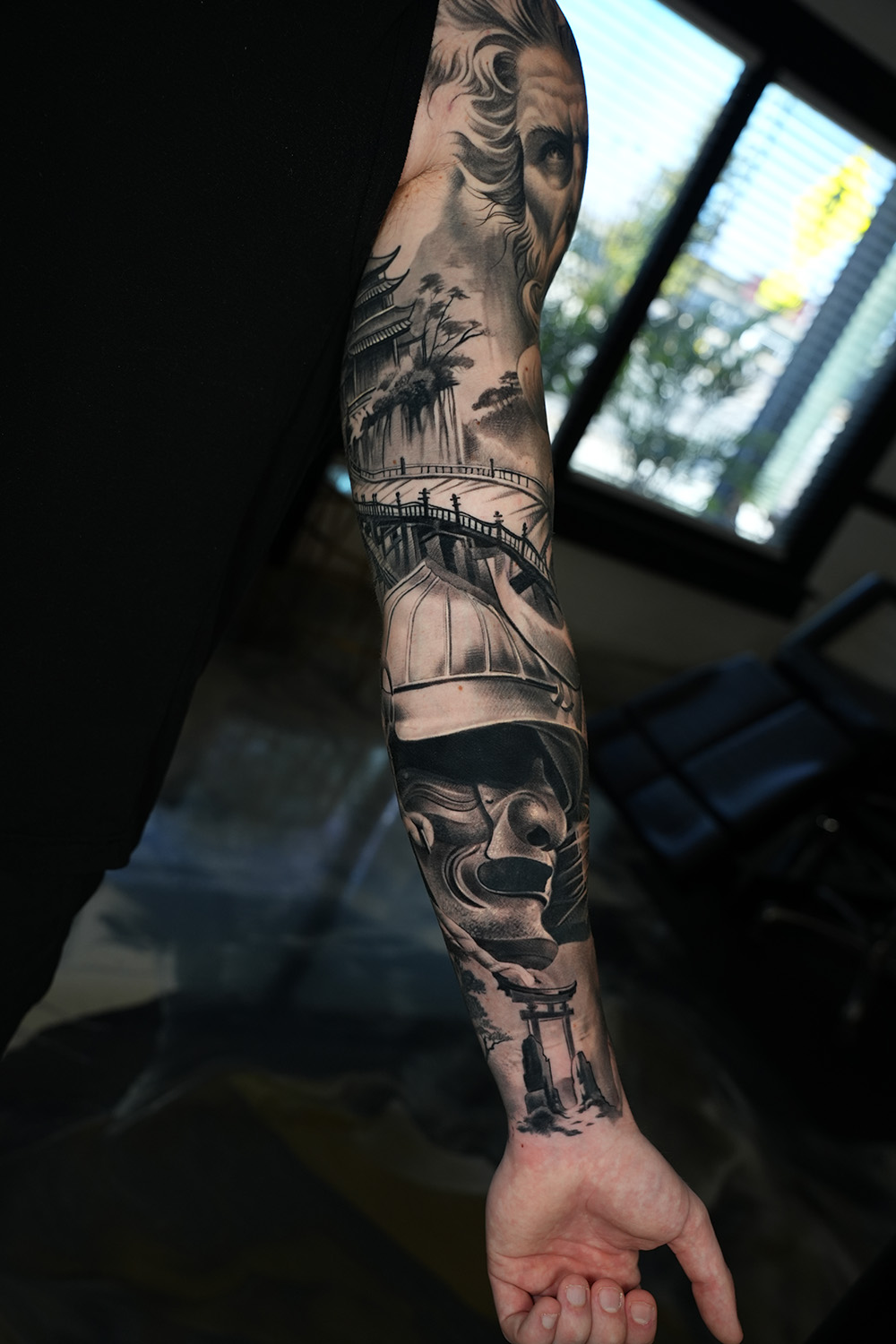 Black and grey realism tattoo of portraits, a bridge and a ship on the full sleeve at The Secret Tattoo Studio in Tampa