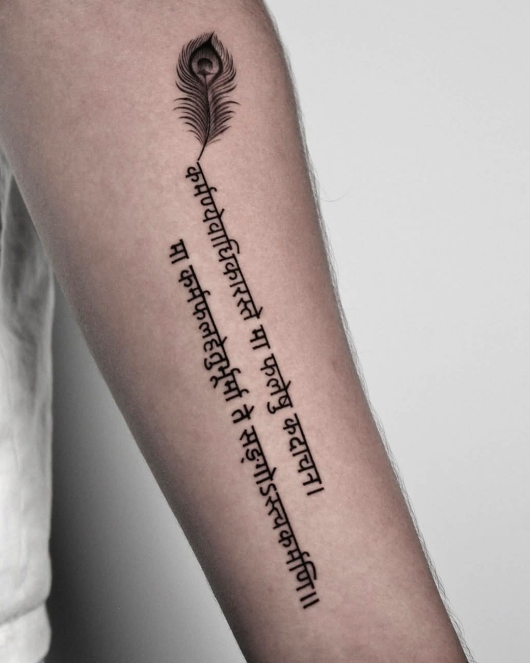 Fineline tattoo of Sanskrit lettering with a peacock feather on the forearm at The Secret Tattoo Studio in Tampa