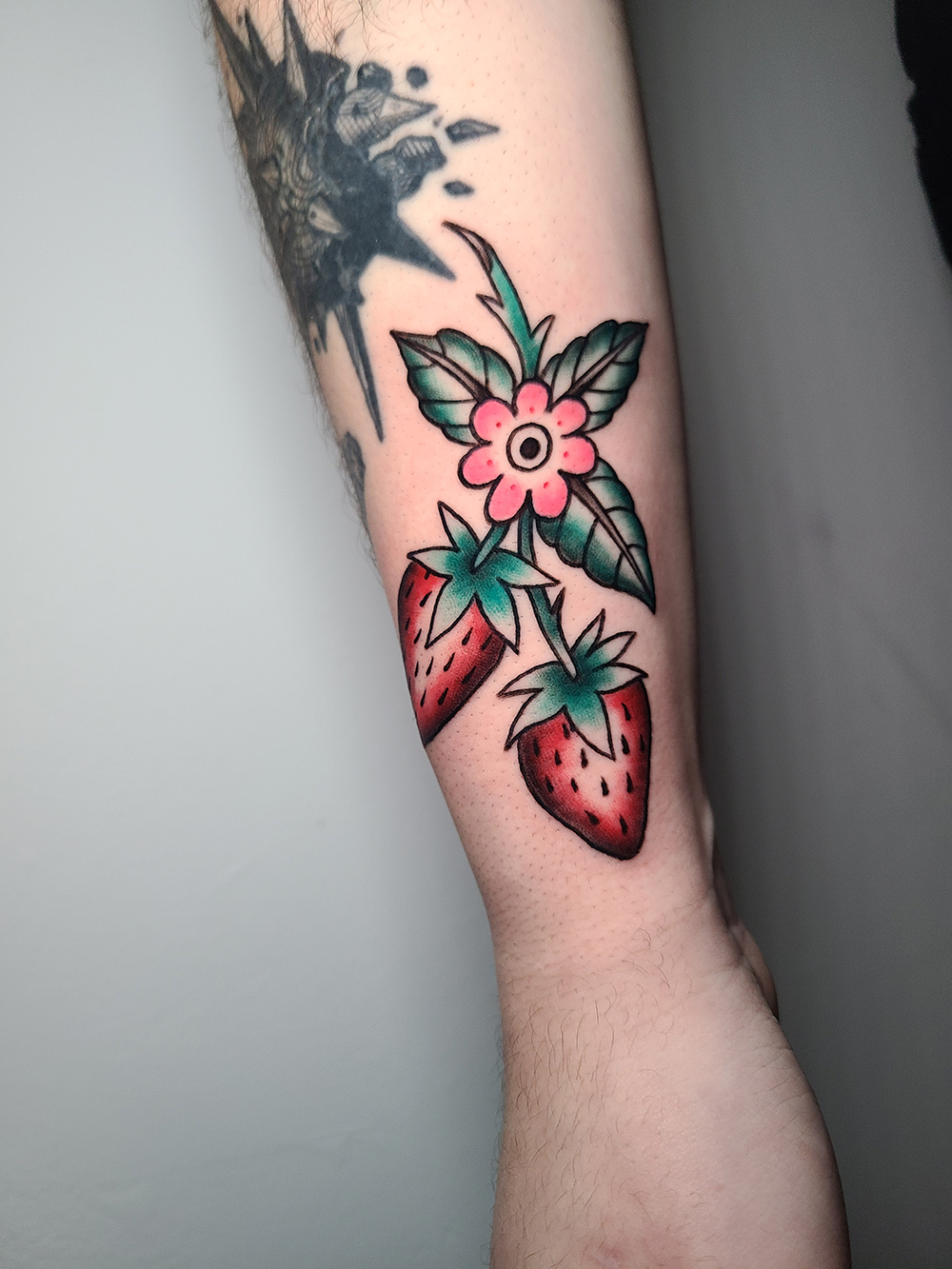 Traditional tattoo of strawberries and a pink flower on the forearm at The Secret Tattoo Studio in Tampa