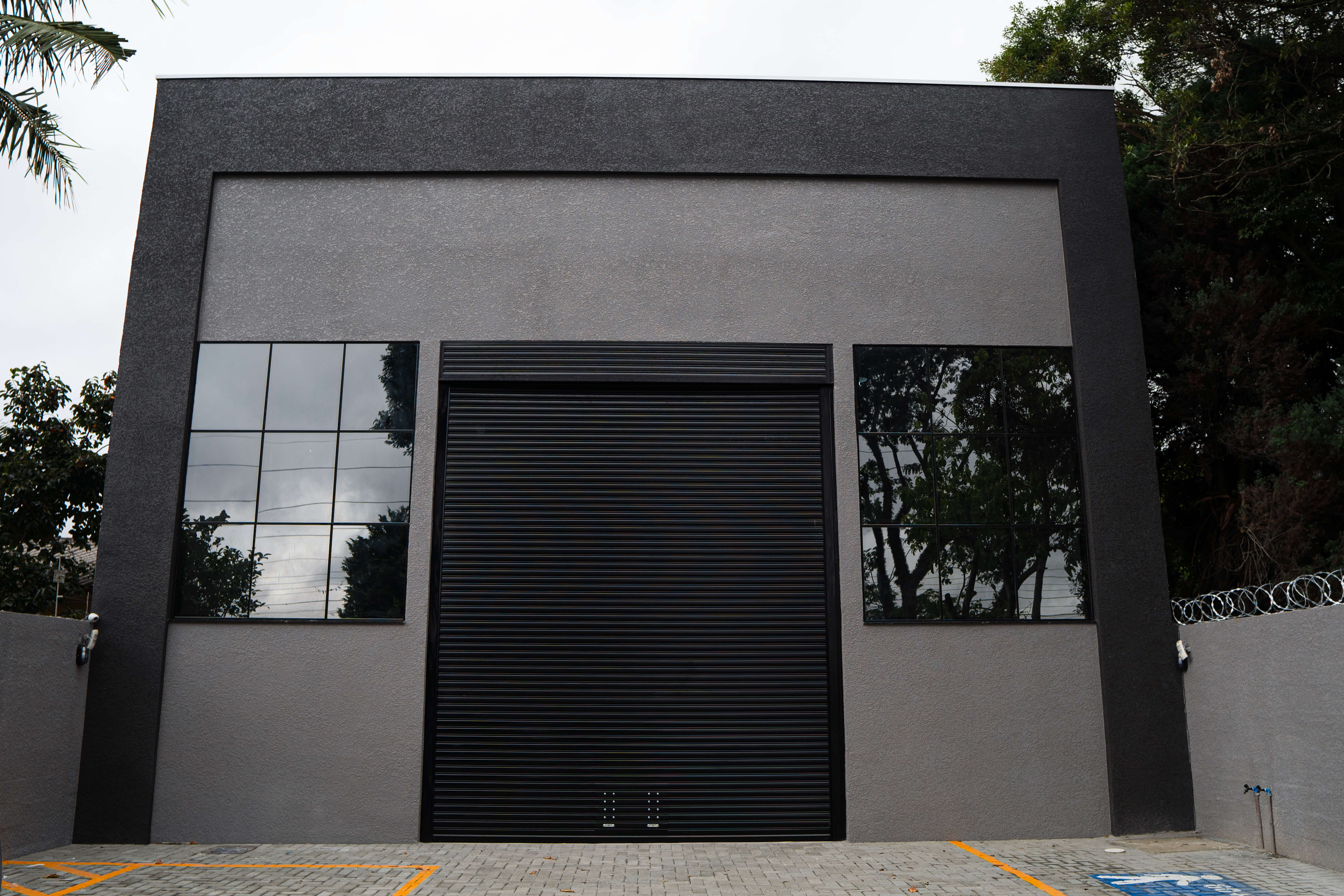 Frente de prédio moderno com porta de aço preta e janelas de vidro refletindo árvores.