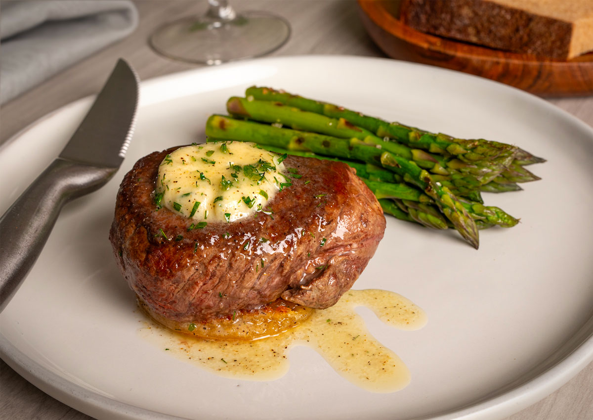 Vacuum-sealed package of organic filet mignon beef from Verde Farms on a beige cloth napkin with peeled potatoes and a sprig of rosemary nearby.