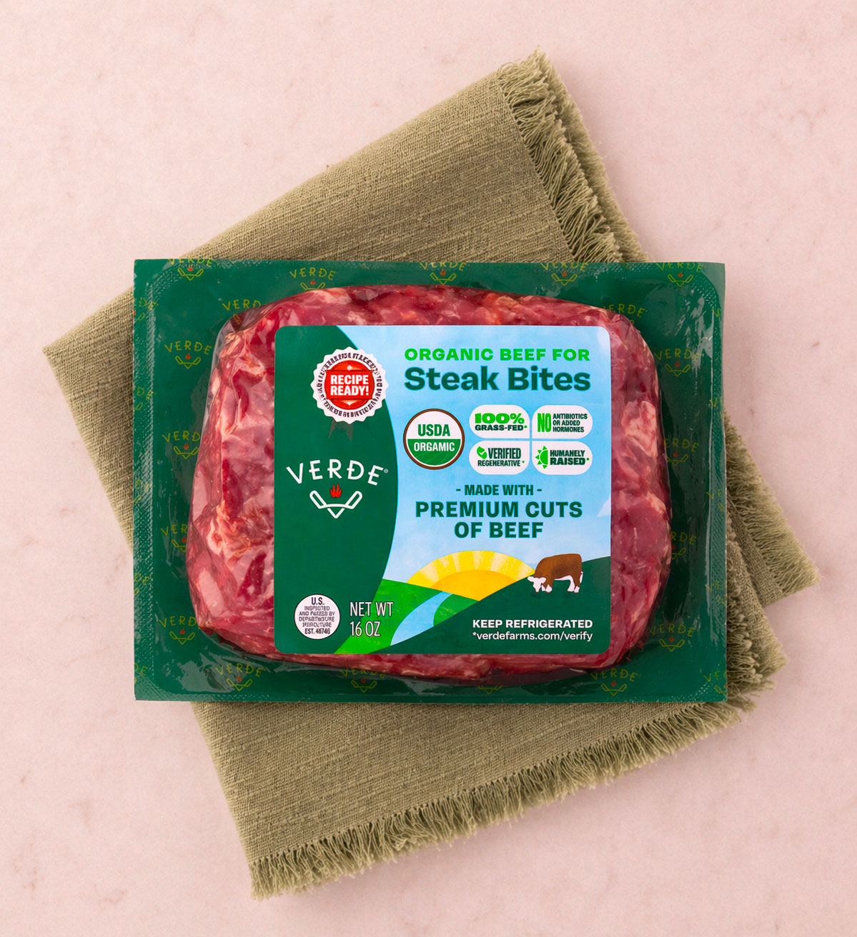 Vacuum-sealed package of organic filet mignon beef from Verde Farms on a beige cloth napkin with peeled potatoes and a sprig of rosemary nearby.