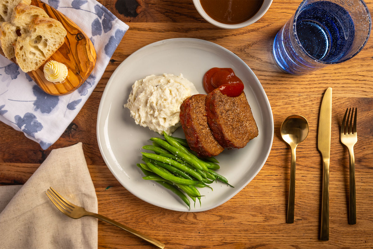 Vacuum-sealed package of organic filet mignon beef from Verde Farms on a beige cloth napkin with peeled potatoes and a sprig of rosemary nearby.