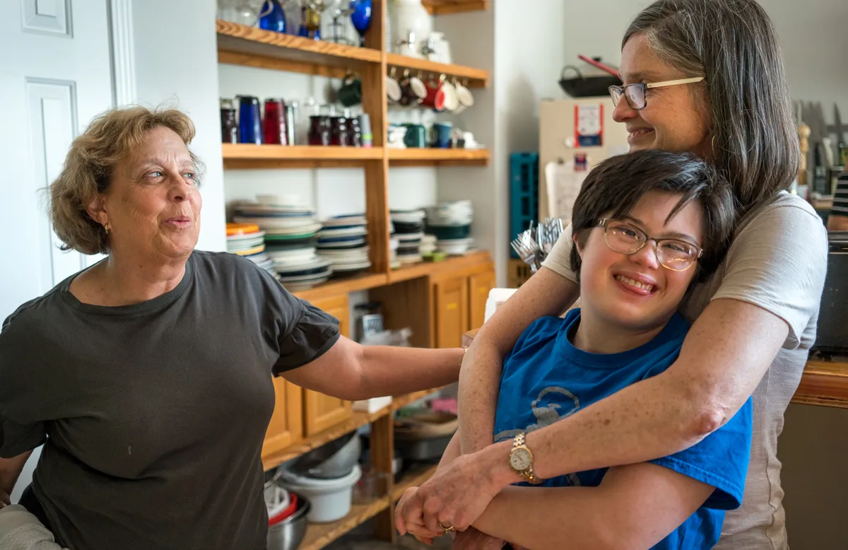 A smiling young person with a disability and her mother, talking to an elderly woman