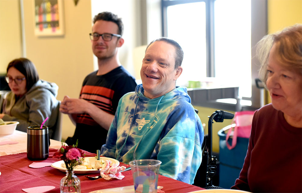 Three people with a disability and an elderly woman sitting at a table at a BLT event