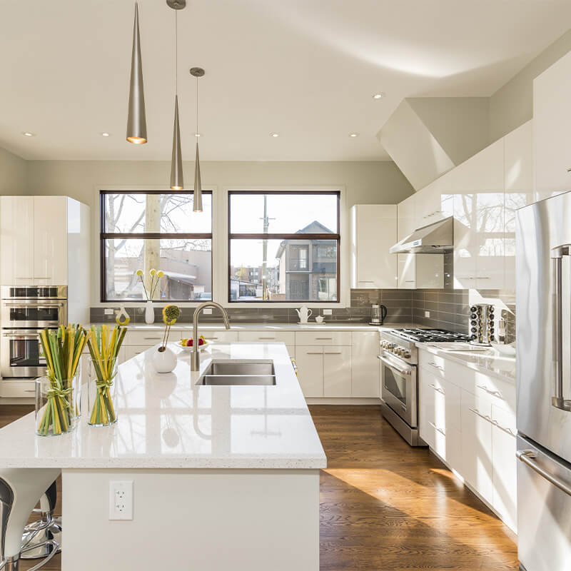 Bright modern kitchen with white cabinets, marble island with sink, stainless steel appliances, and large windows.