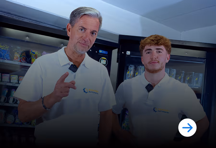 Two men wearing white company polo shirts standing in front of vending machines.
